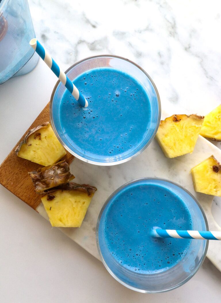 blue smoothie in two glasses with straws and pineapple nearby.