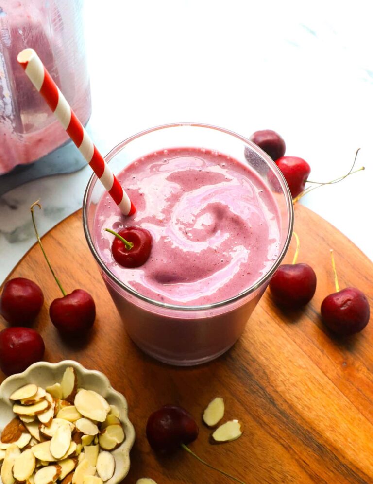cherry smoothie in a glass near a bowl of almonds and cherries.
